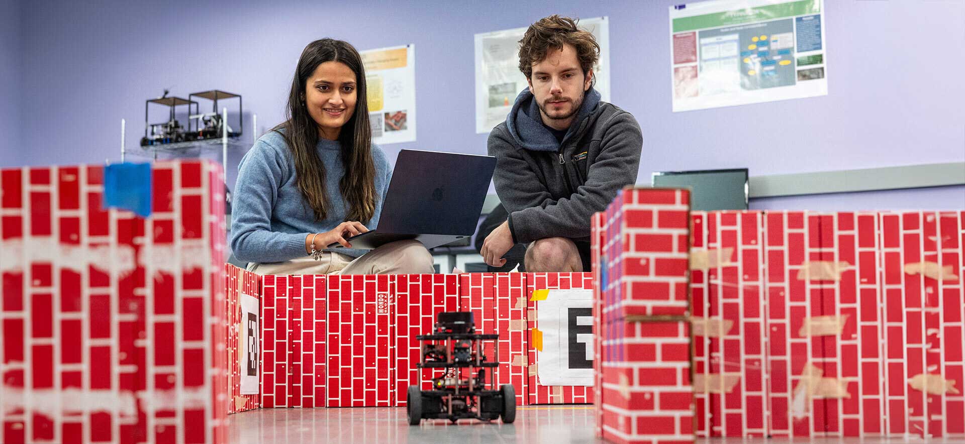 Two students control a robot in a classroom.