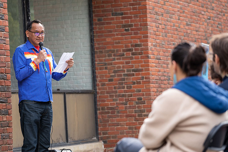 Lee Bitsóí speaks into a microphone to an audience