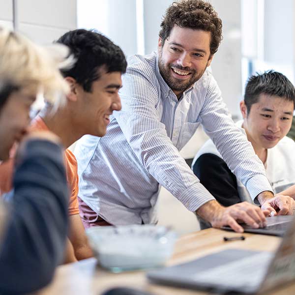 A professor smiles and laughs with students sitting at desks.