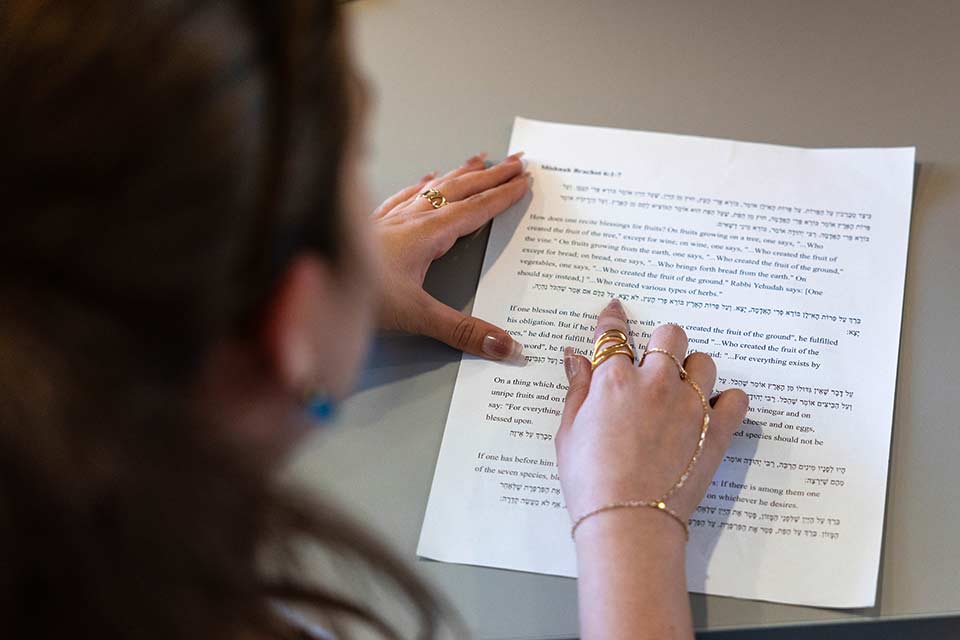 A close up of a hand pointing to a piece of paper with both English and Hebrew,