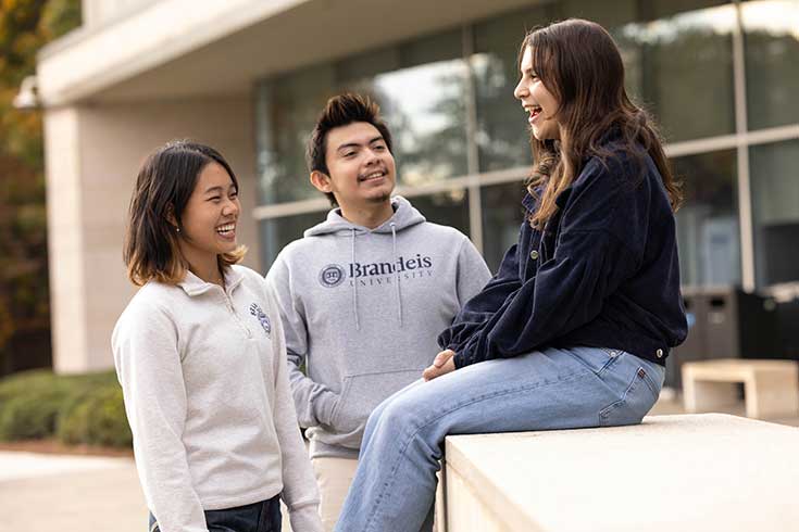 Group of Brandeis students outdoors in sunshine smiles at camera.
