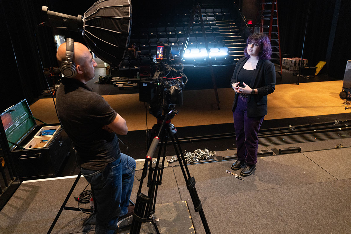 Jae standing on a stage speaking into a camera.