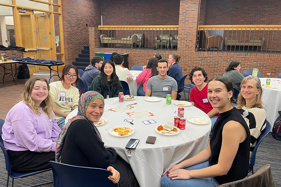 a number of different students and a staff person sitting at a table with a white table cloth and smiling into the camera