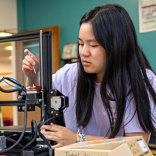 A professor touches a tree as two students look on.