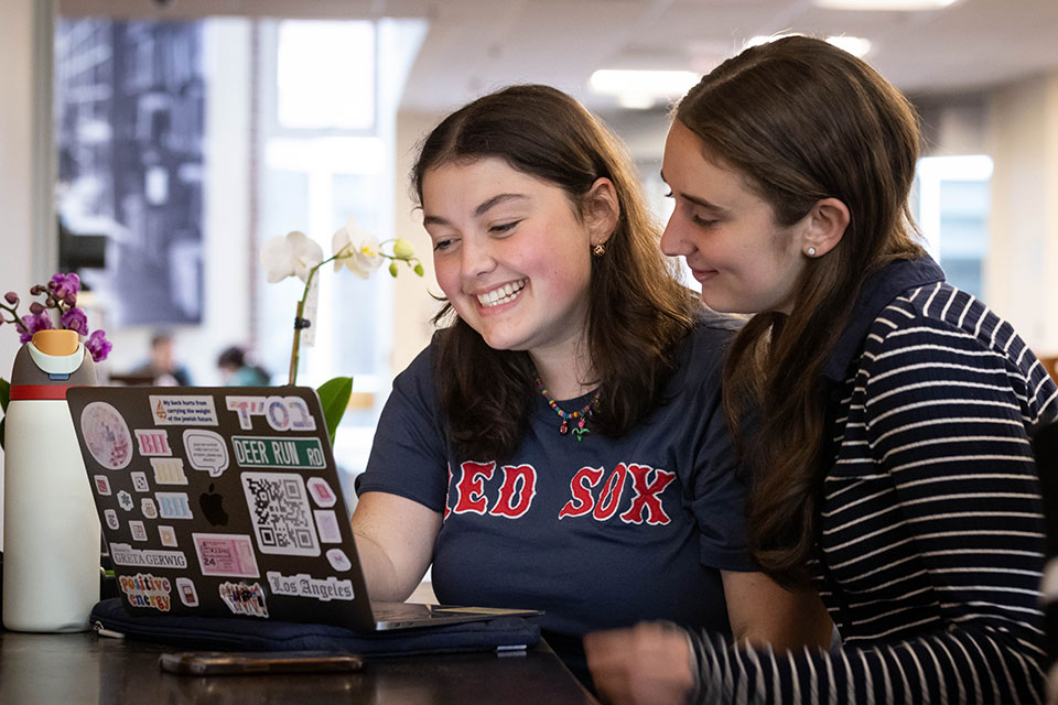 Two students work on a laptop together in the library.