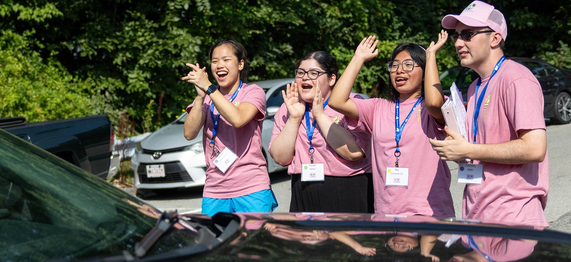 Four students in pink shirts expressing joy around new students moving in to campus.