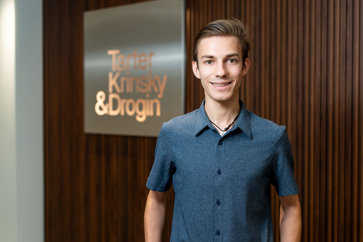 Matthew Pfeffer standing in front of the Tarter Krinsky & Drogin sign at his internship.
