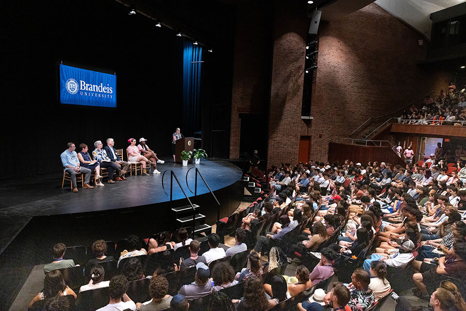 Students in the Spingold Theater at the Orientation University Welcome. Speakers are sitting in chairs on the stage.