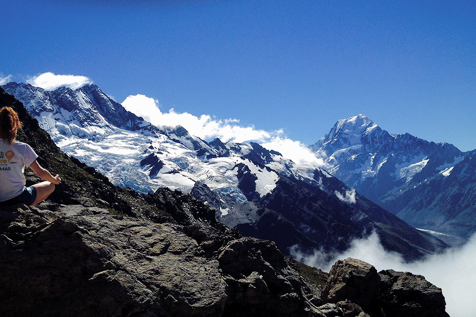 A person sitting on a rock overlooking mountains covered in snow