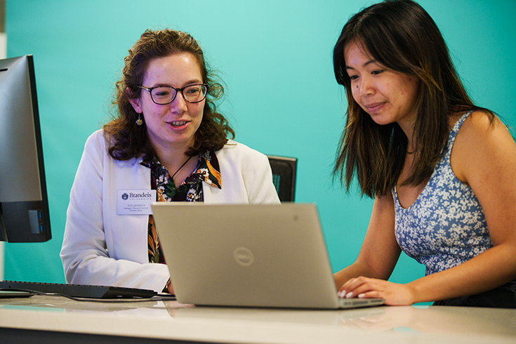 Two students sitting at a table in the library looking at a laptop.