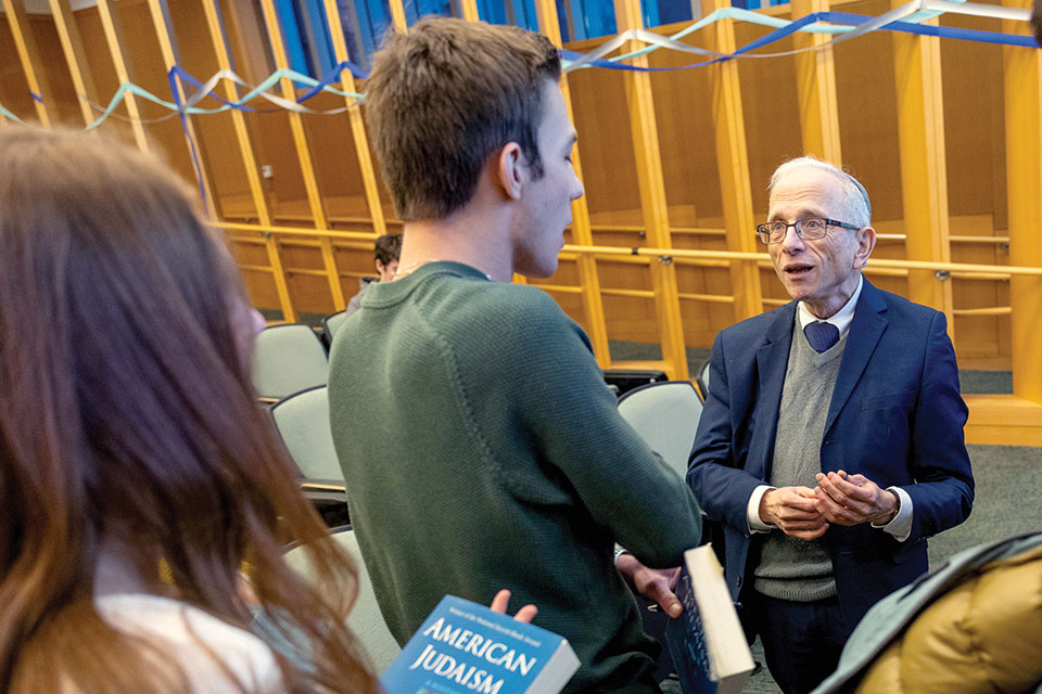 Sarna stands in a classroom and speaks with a group of students.