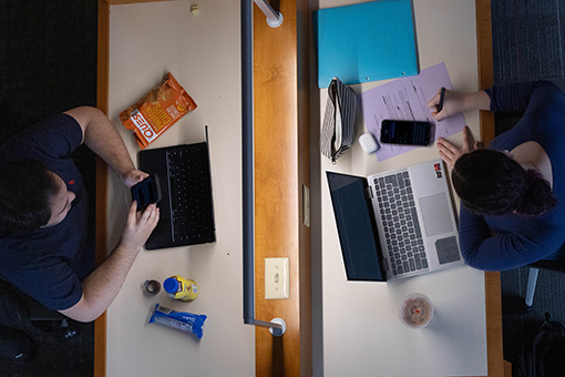 Aerial view of two students working on their laptops in study cubicles that face each other with a divider in the middle.