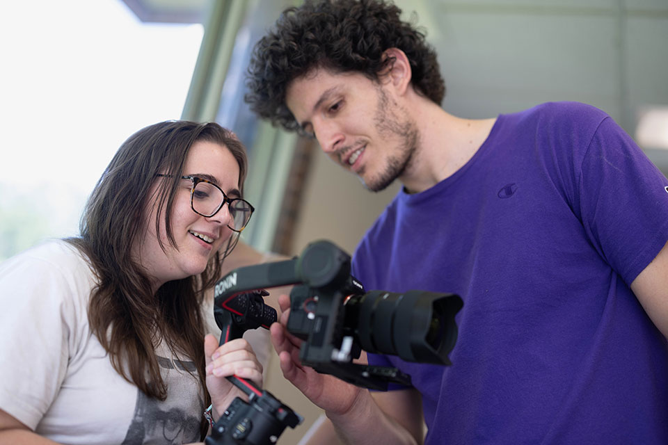 A professor and student look into a camera.