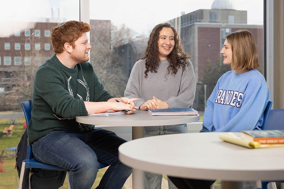 Three students sit and talk at a table at Brandeis University.