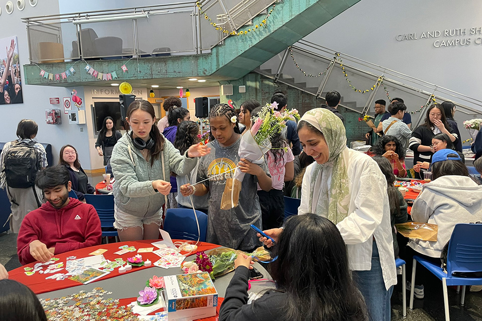 a room with many students doing activities at different tables, standing and sitting, holding flowers